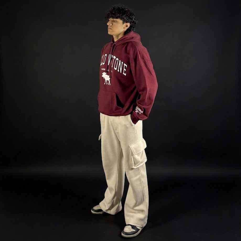 Person wearing a maroon hoodie with white text and beige pants on a black background