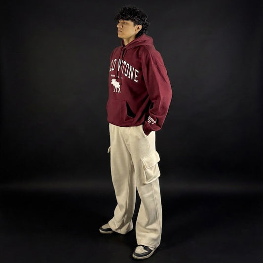 Person wearing a maroon hoodie with white text and beige pants on a black background
